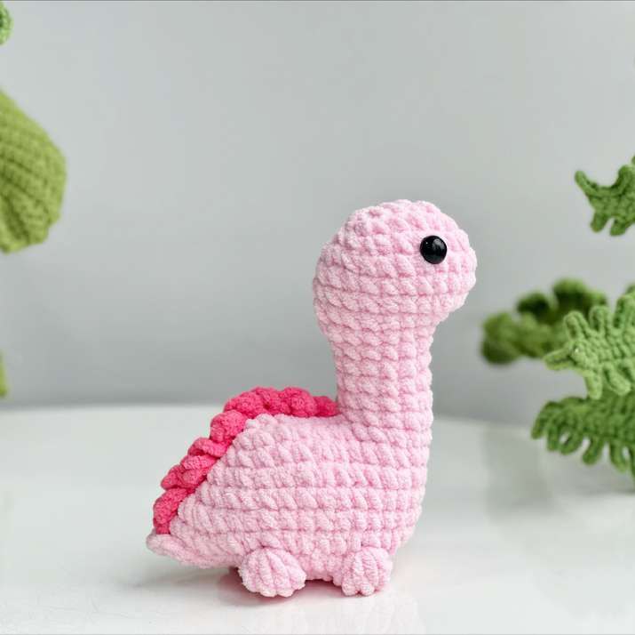 Finished pink crochet brachiosaurus with a long neck, black eyes, bobble feet and dark pink spikes