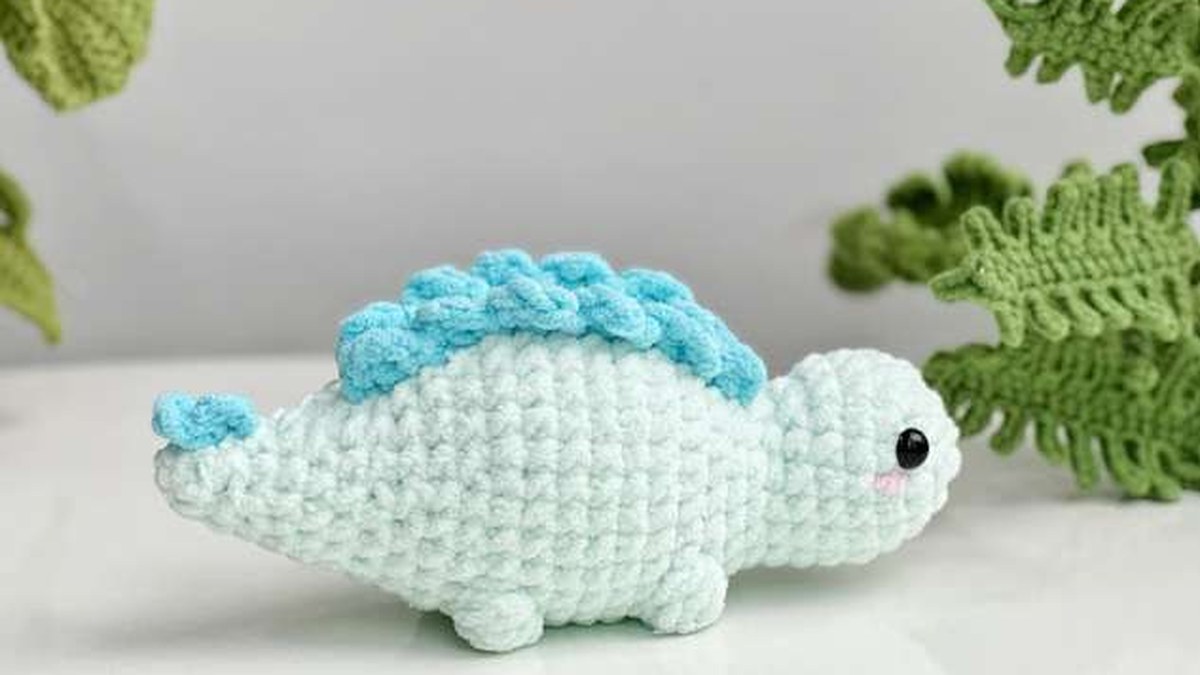 Mint no-sew crochet stegosaurus with blue back plates, next to crochet ferns