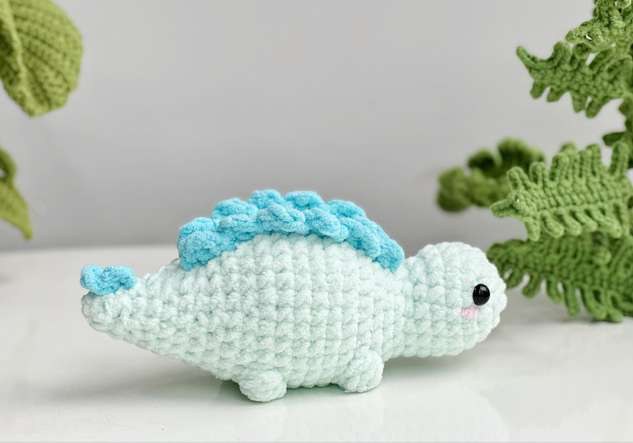 Finished mint crochet stegosaurus with two rows of blue back plates, bobble feet and a spiky tail