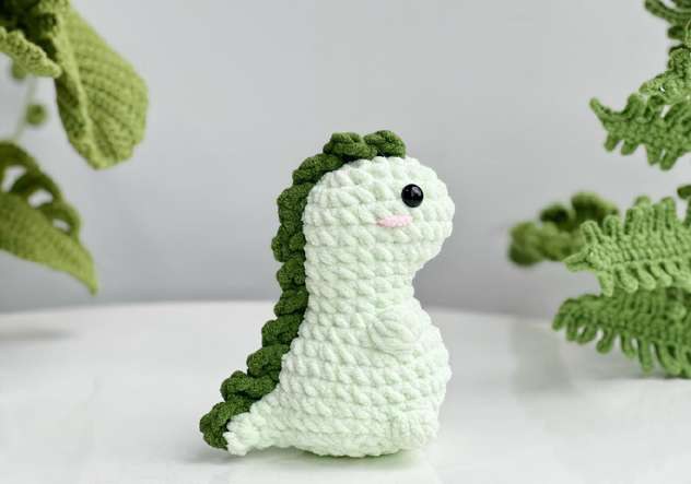 Finished pale green crochet T-rex sitting upright with dark green spikes down its back