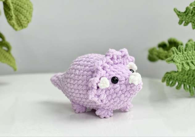 Finished purple crochet triceratops with a scalloped frill, three white horns and bobble feet